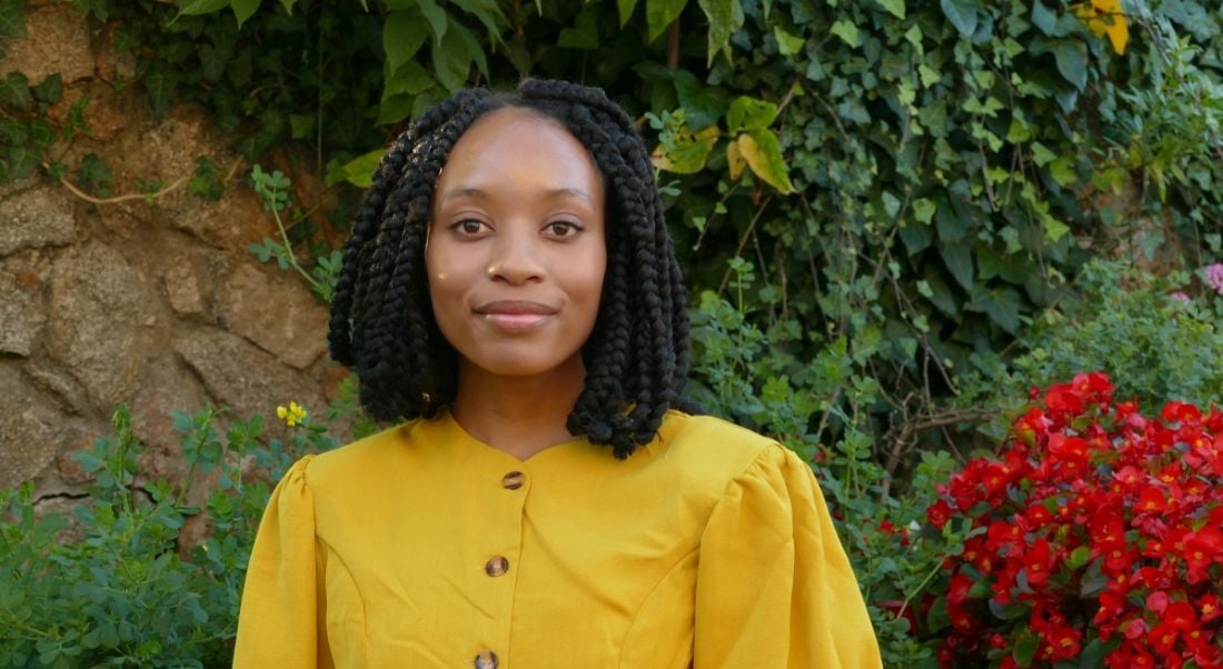 Reabetswe Zwane, who is doing a PhD in computational chemistry, is standing outdoors and smiling into the camera while wearing a bright yellow top.