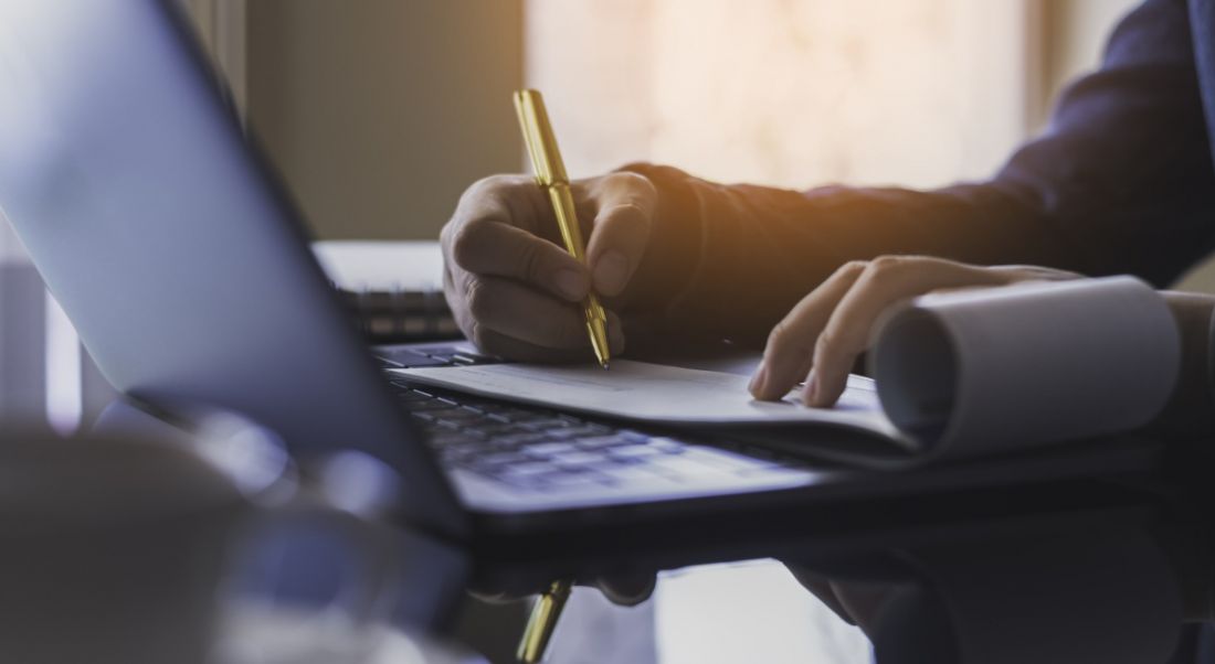 A person working on a payroll document while also working on a laptop.