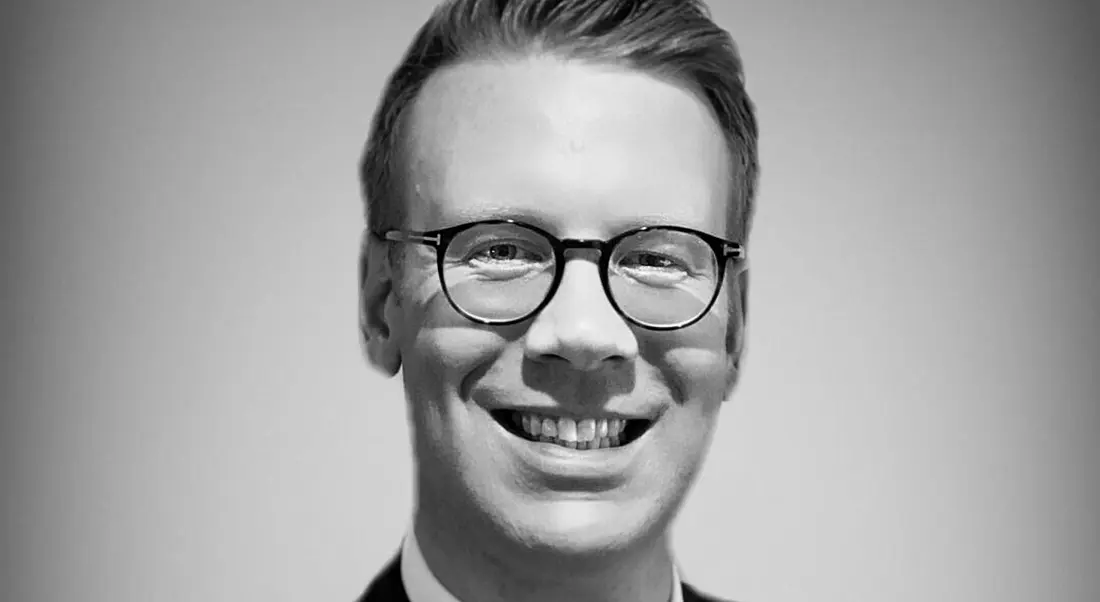 A black-and-white headshot of Samuel Schofield smiling into the camera.