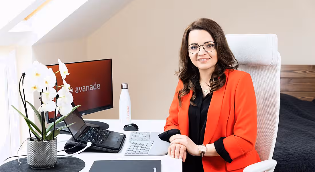 Aga Wiszniewska of Avanade is sitting at her work set-up at home. She is wearing a red blazer and smiling into the camera.
