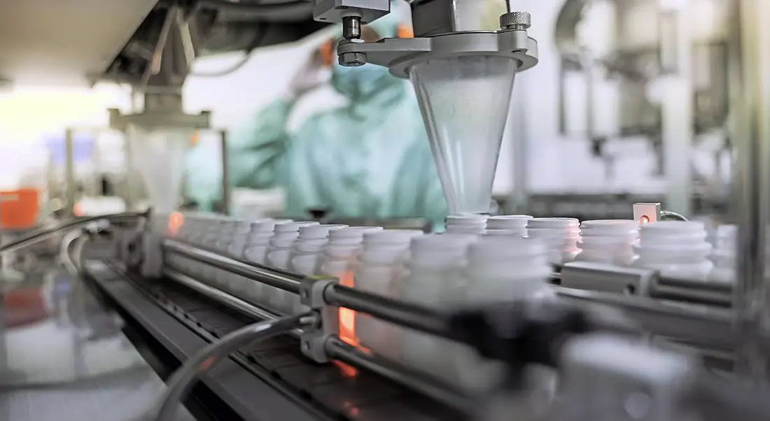 A bioprocessing facility showing the transfer of medicine bottles on a conveyor belt in a pharmaceutical setting.