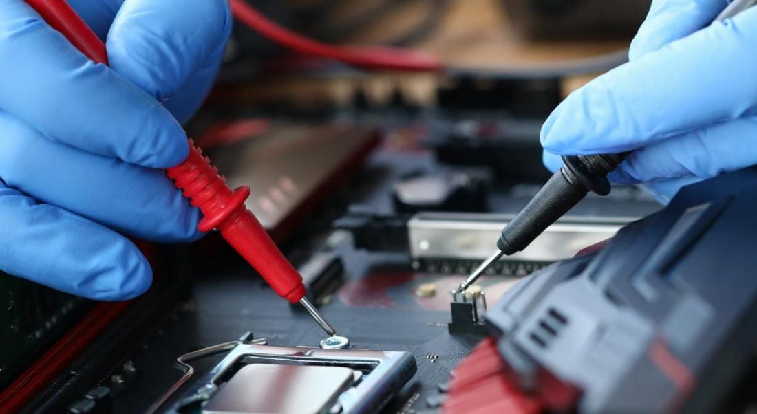 A close up of hands wearing blue protective gloves holding tools, working on an electronic device.