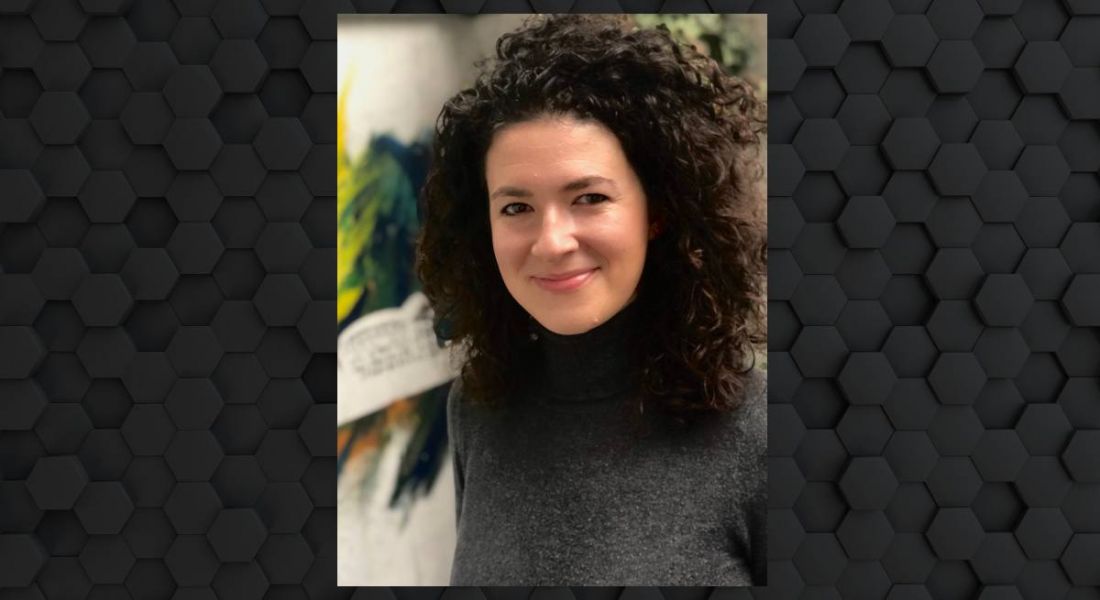 Hannah Herlihy Lowe, head of customer success at Conjura, is smiling into the camera. She has dark curly hair and is wearing a charcoal polo-neck.