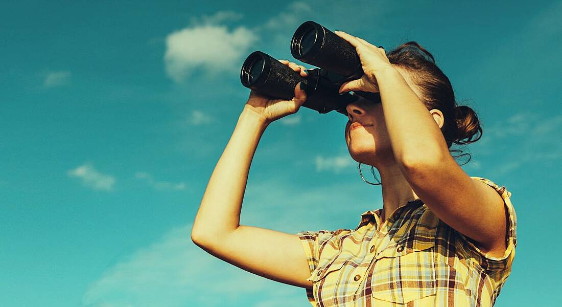 A woman looking through her binoculars against a blue sky.