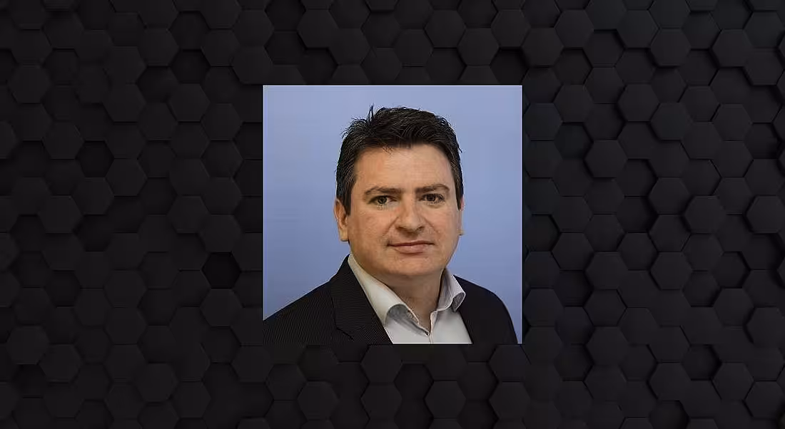 A headshot of a man in a suit against a black background.
