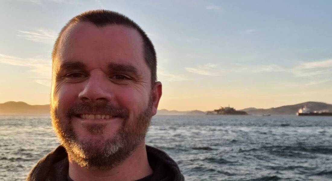 A close-up of Noel Crowley of Fidelity Investments smiling at the camera with the ocean in the background at sunset.