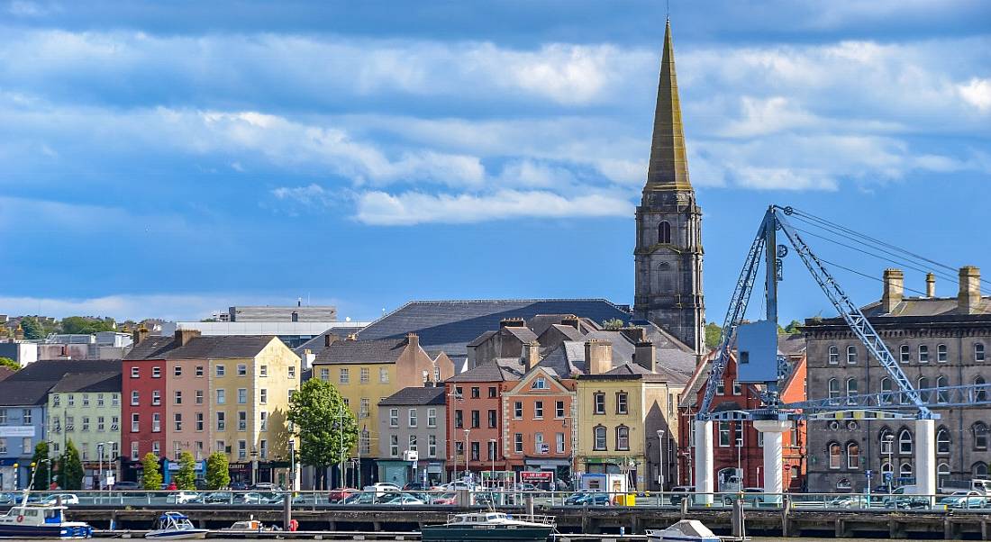 Waterford cityscape from across the River Suir. You can see a row of colourful buildings and a tall church steeple.