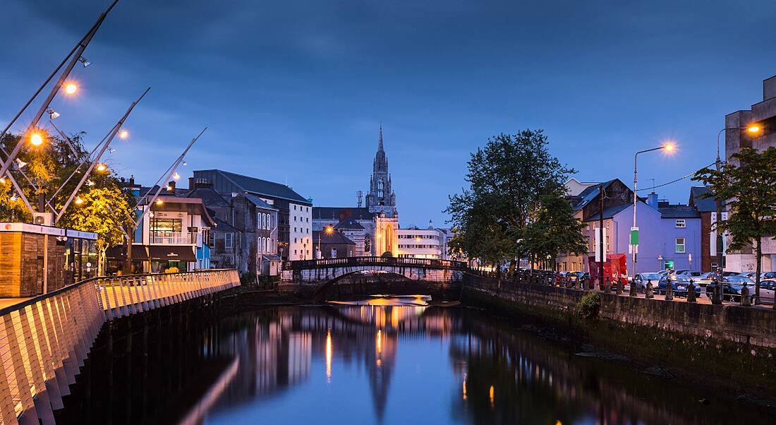 The River Lee in Cork city at dusk, with buildings lit up either side of the docks.