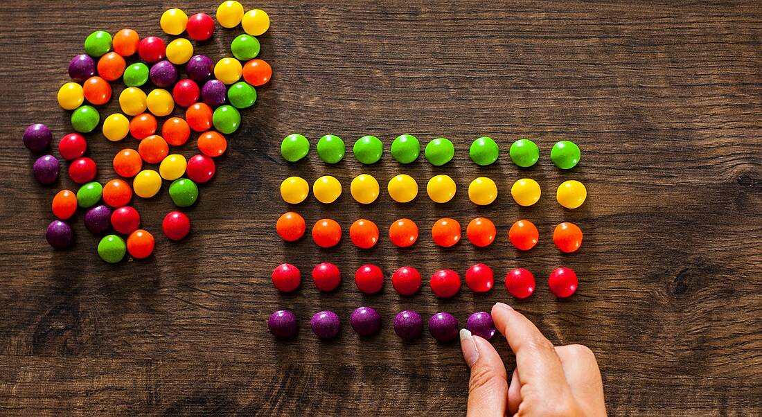 A hand takes different coloured sweets from a pile and puts them in perfect, matching lines, symbolising a perfectionist mindset.