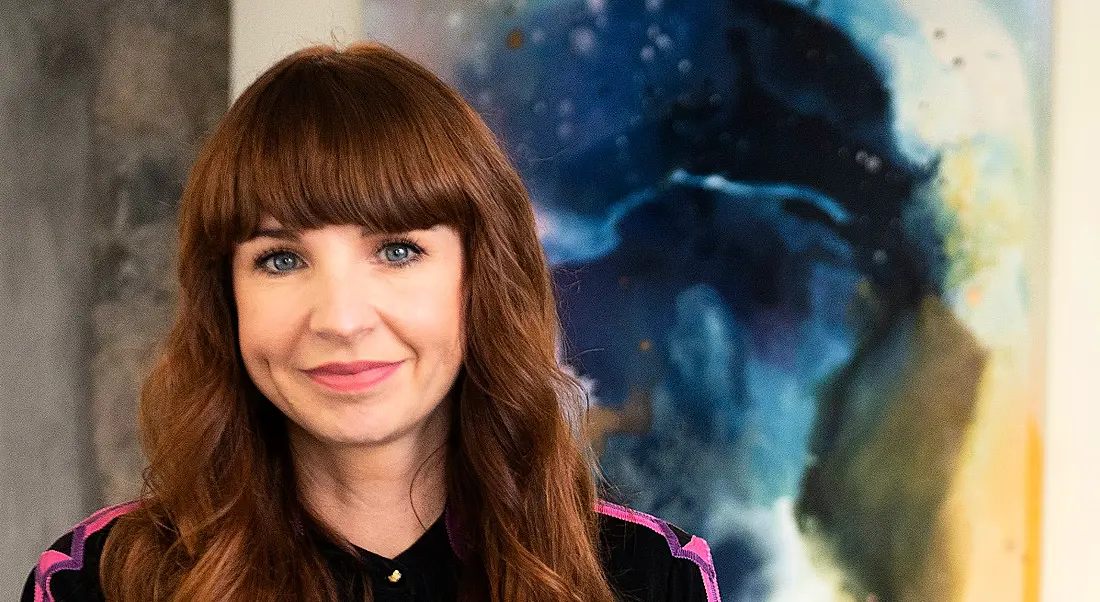 A woman smiling at the camera with a colourful print in the background.