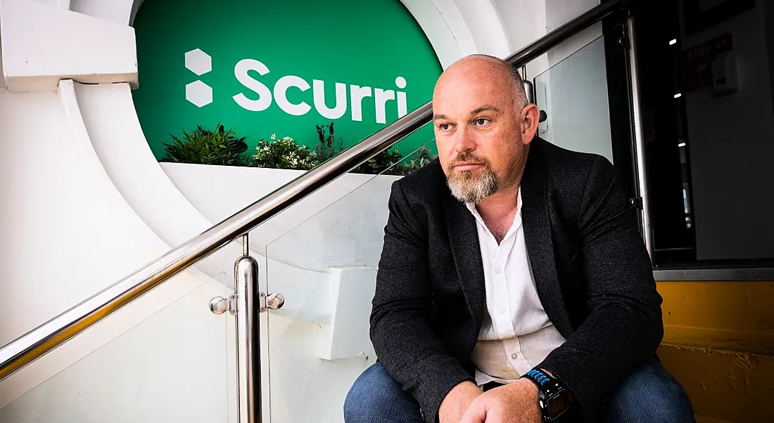 Scurri founder Rory O’Connor sits on a staircase next to a green Scurri logo.