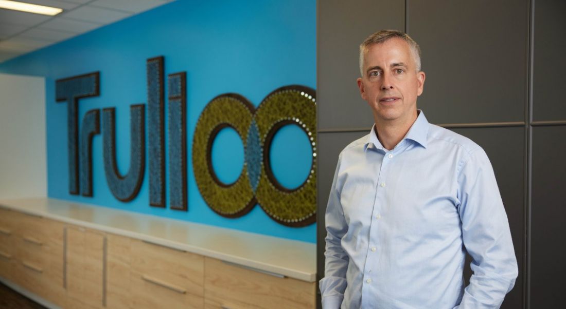 A man in a shirt stands in an office in front of a sign that says Trulioo.