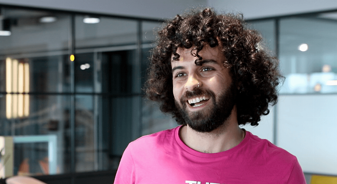 A man in a pink T-shirt smiles at the camera in a brightly lit Zalando office.