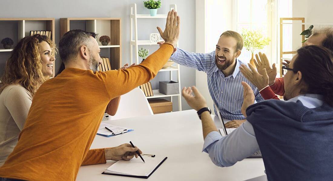 A group of people around a boardroom table cheering and high-fiving.