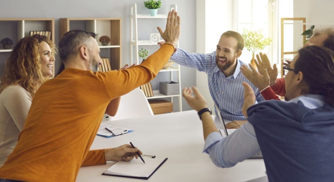 A group of people around a boardroom table cheering and high-fiving.