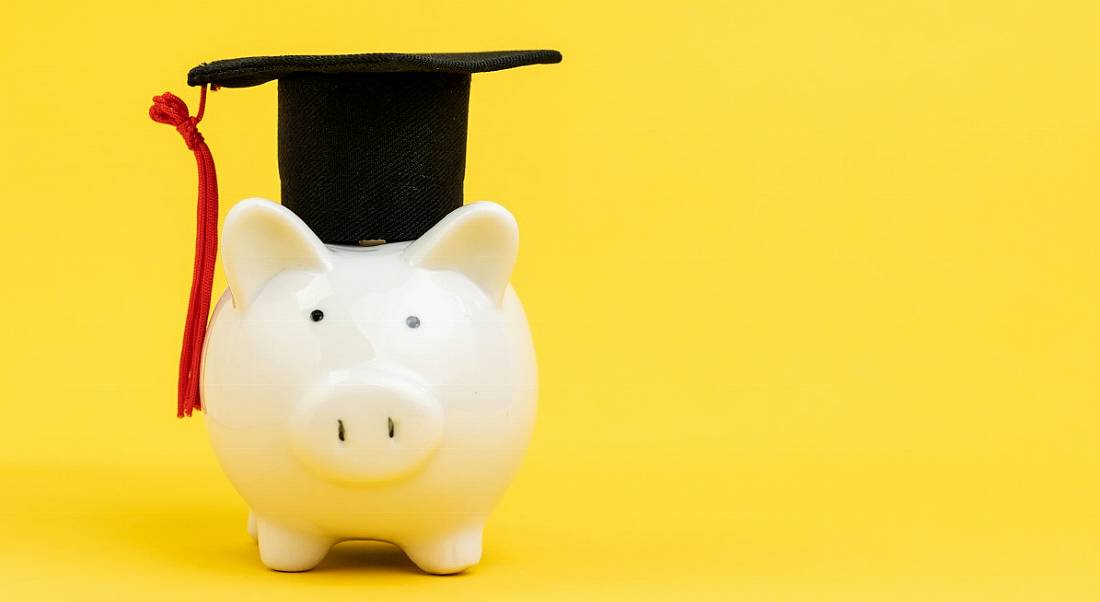 A white piggy bank wearing a graduation cap against a yellow background.