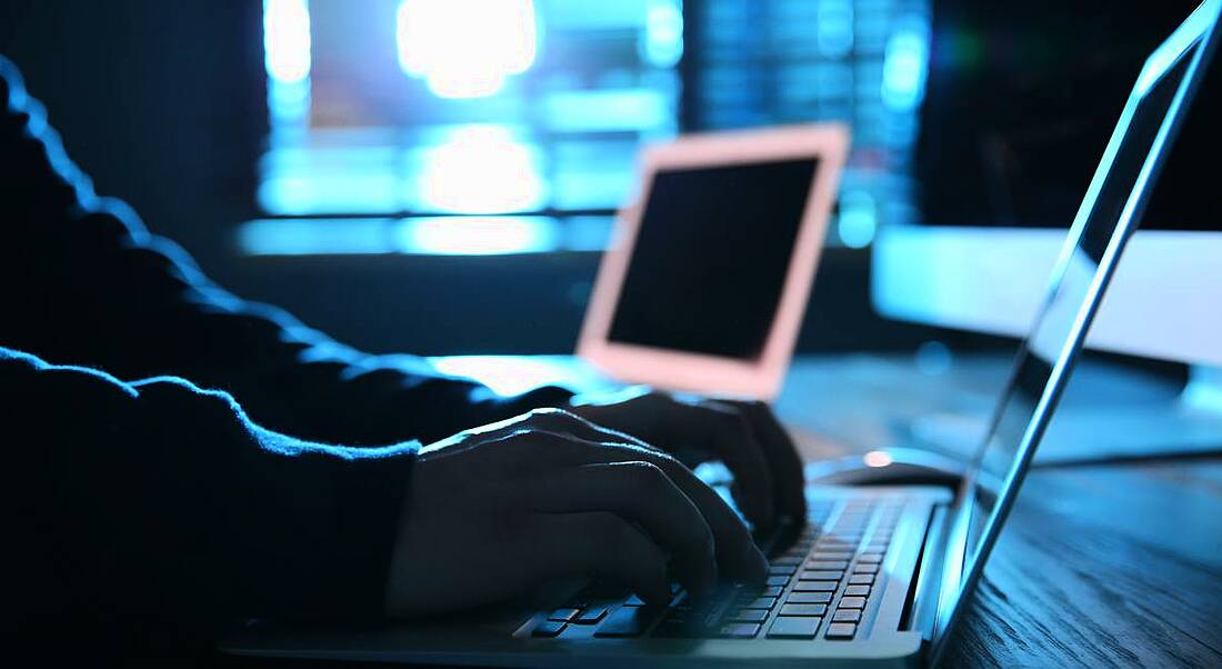 Hands typing on the keyboard of a laptop in a dark room, symbolising harmful online content, which Moonshot is trying to tackle.