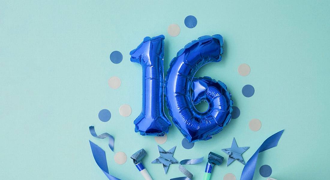 Two foil blue balloons spelling the number 16. It’s surrounded by blue confetti against a mint green background.