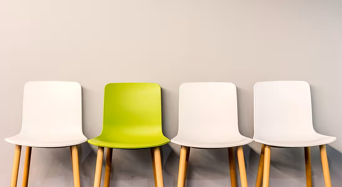 A row of chairs lined up for job interviews. Three of the chairs are white and one is lime green.
