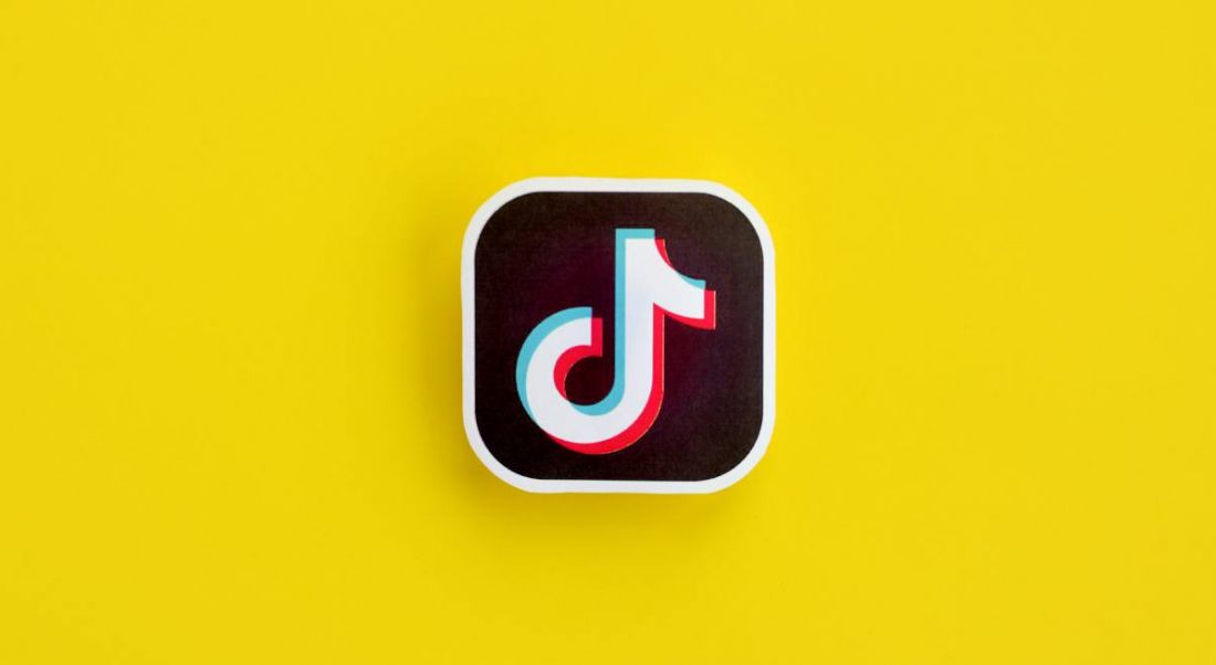 A paper logo for TikTok, which resembles a music note, on a bright yellow background.