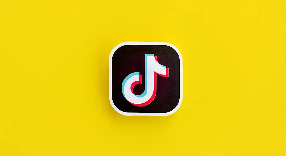 A paper logo for TikTok, which resembles a music note, on a bright yellow background.