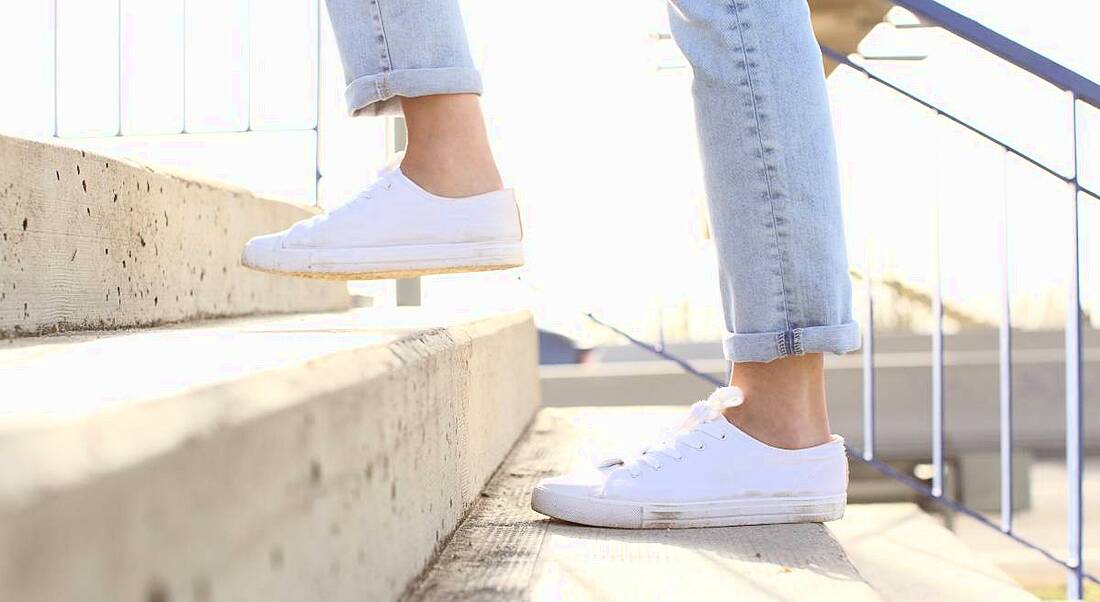 Close up shot of woman's legs as she climbs a concrete staircase. She is wearing ankle-length jeans and white plimsolls.