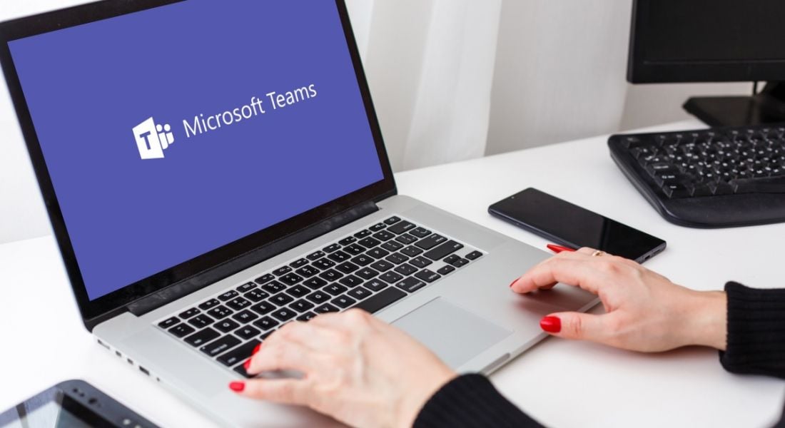 Woman's hands hovering over the keyboard of a laptop displaying the Microsoft Teams logo