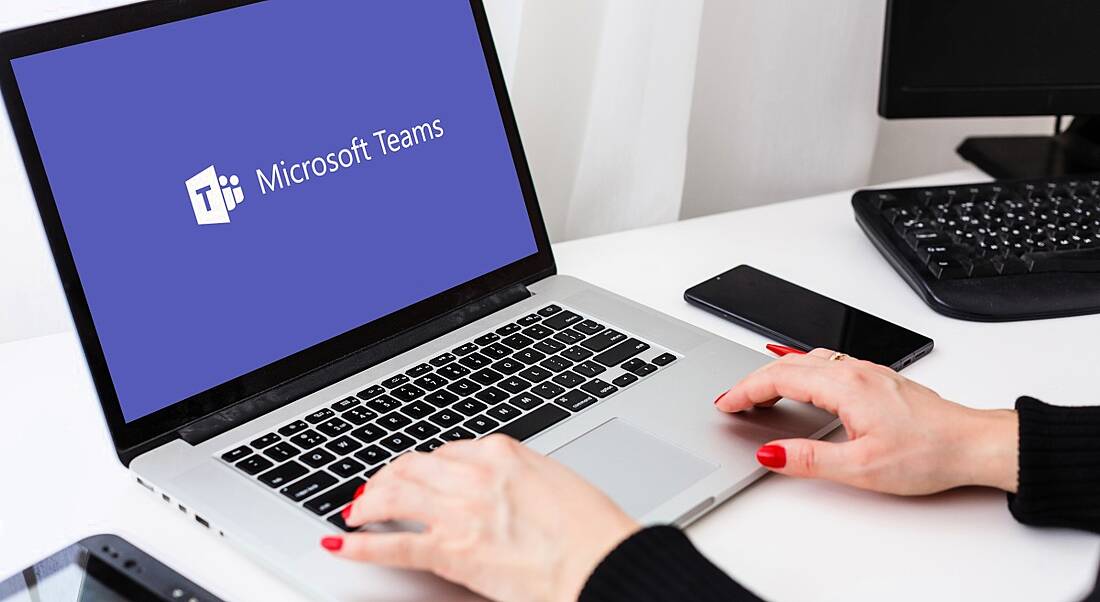 Woman's hands hovering over the keyboard of a laptop displaying the Microsoft Teams logo