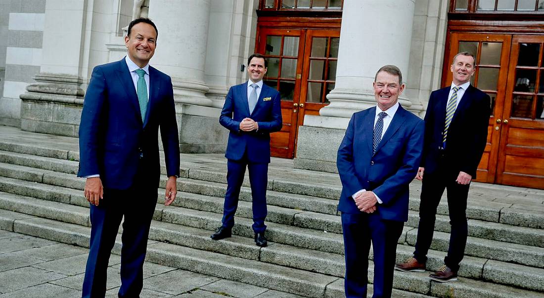 Four men in suits stand outside Government buildings.