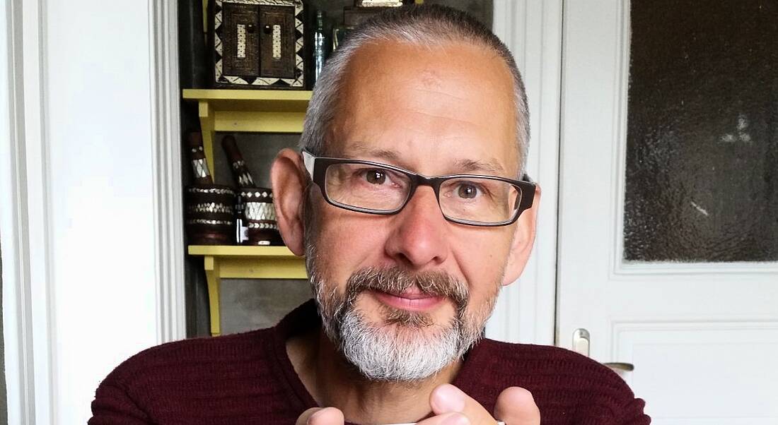 A close-up of a man with glasses smiling at the camera.