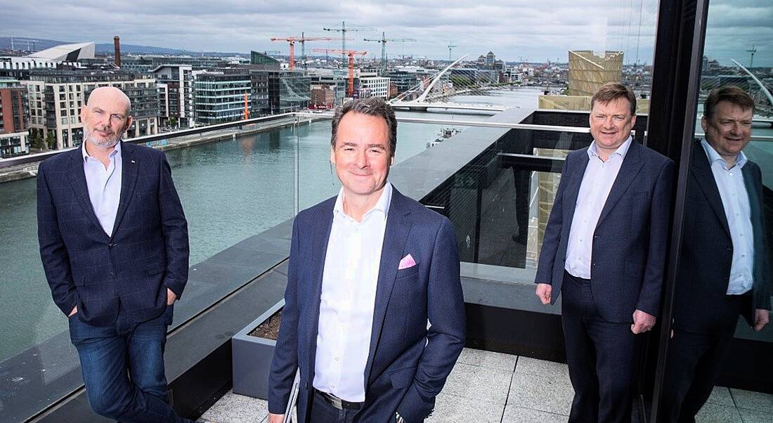 Three men stand on a balcony overlooking the Dublin docklands.