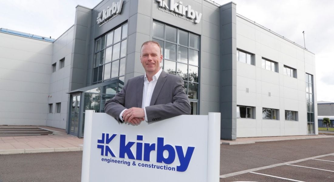 Ruairi Ryan stands outside the premises of Kirby Group Engineering in Raheen Business Park, holding up a sign bearing the company’s logo.