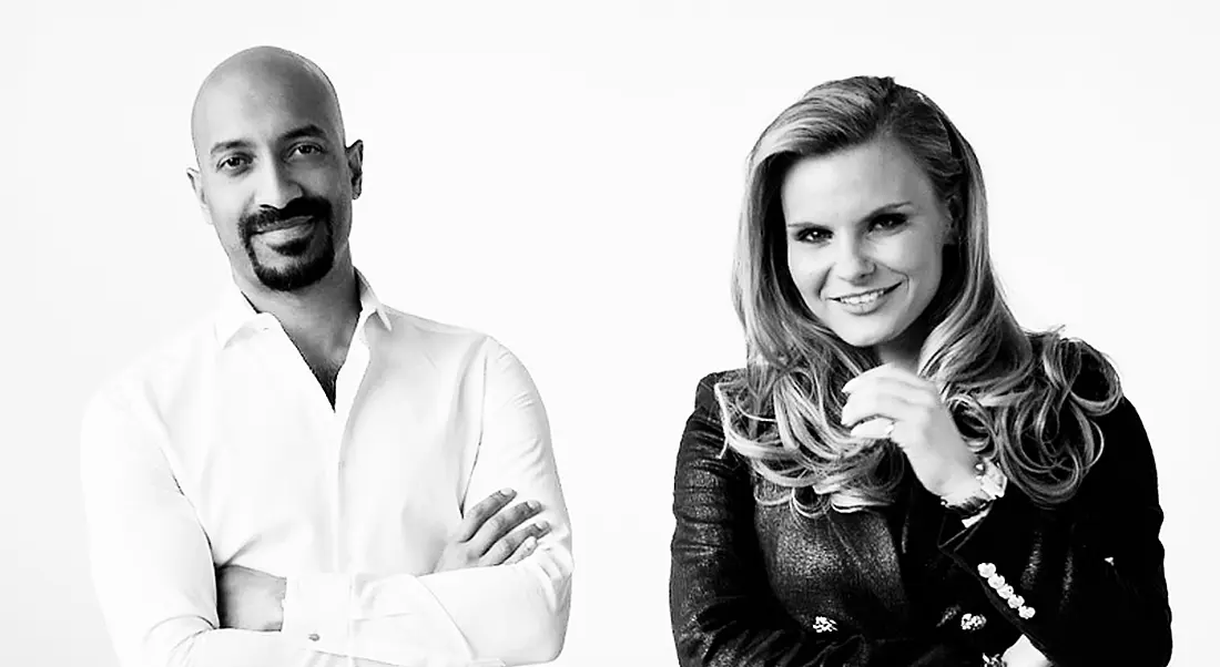 A black-and-white image of a man and woman, both standing with their arms folded, smiling at the camera.