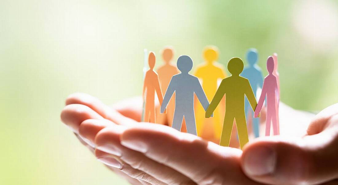 Hands cupped holding a bunch of different coloured paper dolls that are standing up holding hands in a circle to symbolise diversity.