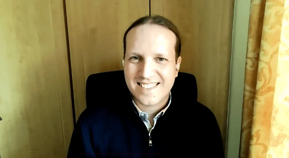 A man sitting in a desk chair smiling at the camera. He is Alex Ferreira of Avanade Ireland.