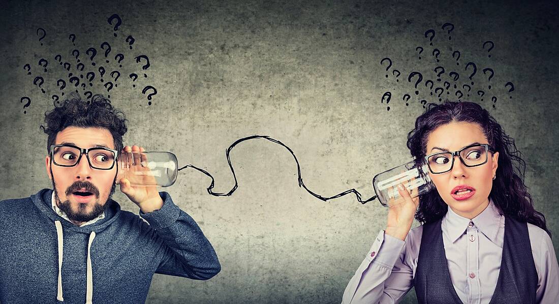 Man and woman standing far apart dressed for the office holding two cans to their ears as if talking with them, connected by string.