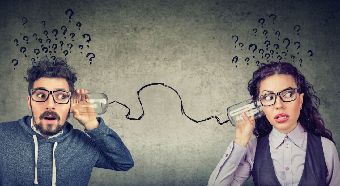 Man and woman standing far apart dressed for the office holding two cans to their ears as if talking with them, connected by string.