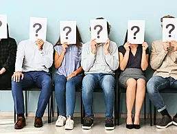 A row of office workers, one behind the other, sit at their desks in front of computers with their heads in their hands. They are tired and working overtime. It is dark outside.