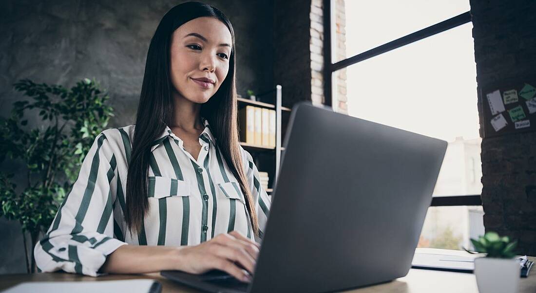 Woman working at her laptop beside a window in a home office.