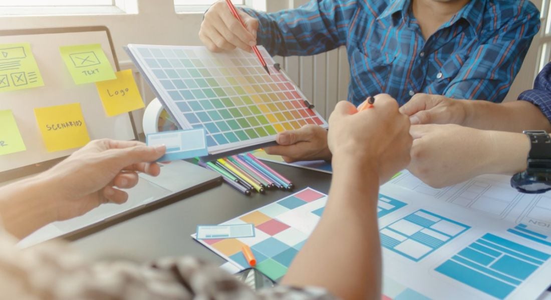 A group of people sit around a table, picking out colours and features to design a website.