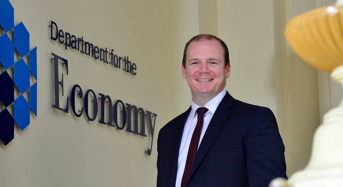 Northern Ireland economy minister Gordon Lyons stands alongside a wall with lettering that says department for the economy.