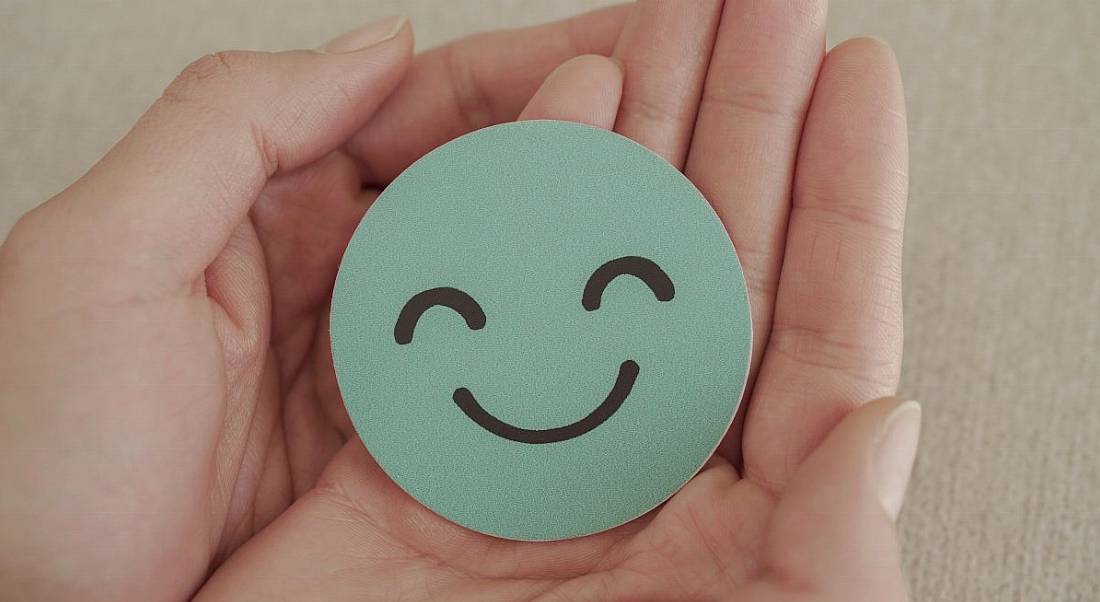 A pair of hands holding a round, blue piece of paper with a smiley face on it.