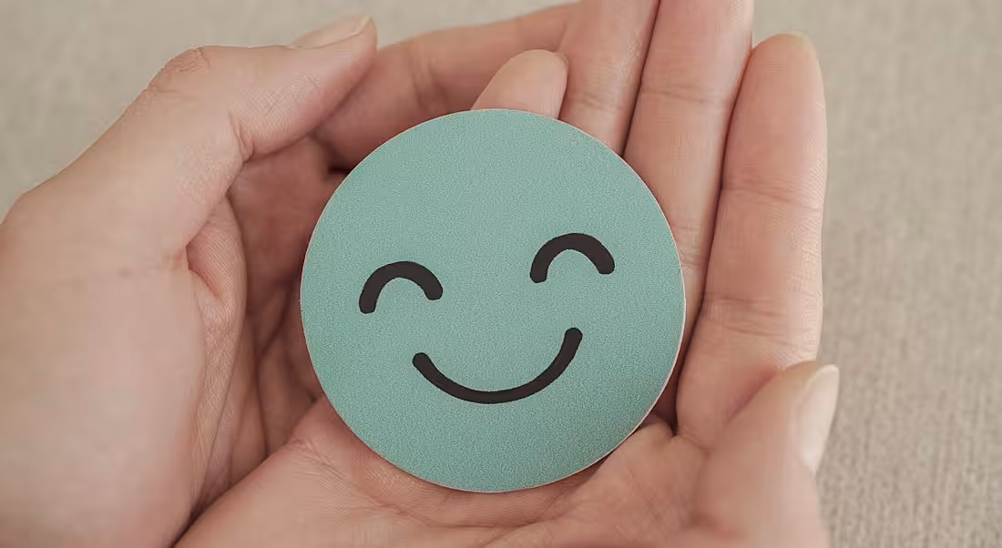 A pair of hands holding a round, blue piece of paper with a smiley face on it.