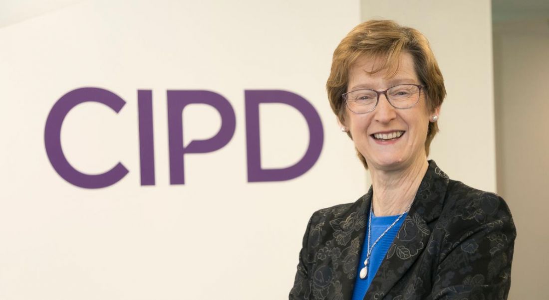 A woman with short hair wearing a black blazer with arms folded smiling at the camera in front of a wall that says CIPD in purple lettering.