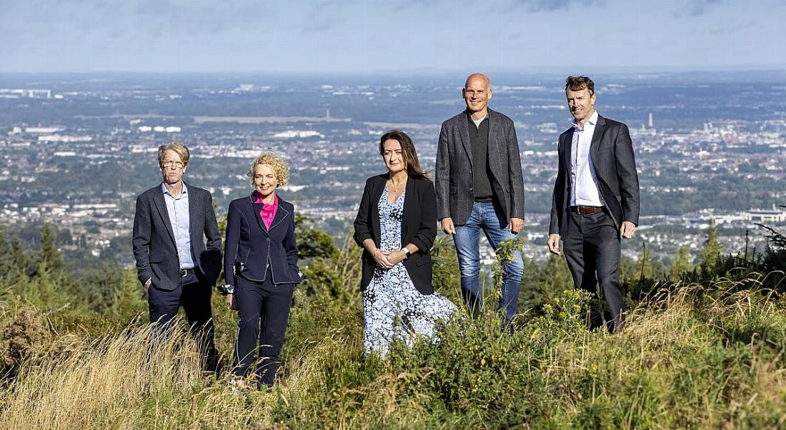 Five people stand on a hill with a view of Dublin behind them.