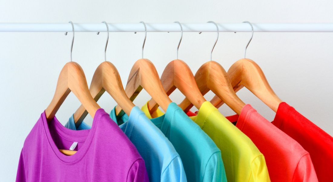 A row of T-shirts hanging on a rail in a rainbow of colours.