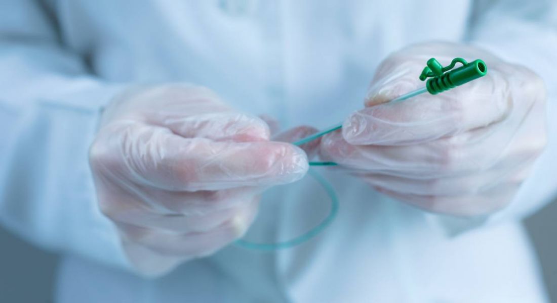 A doctor wearing gloves and a protective smock handles a catheter tube.