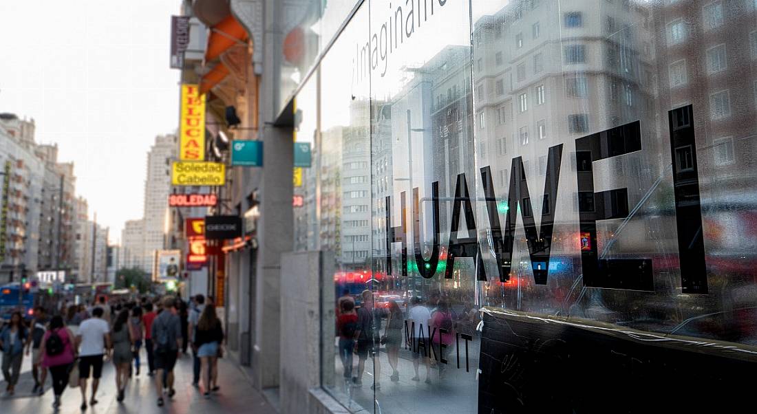 People walk past Huawei offices bearing the company name in a busy street.