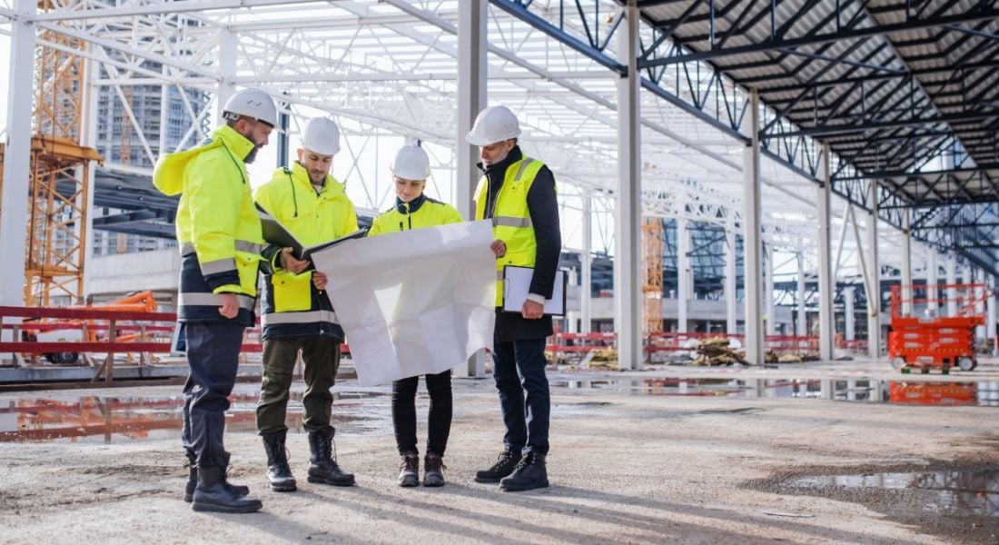 Group of four engineers gathered in a group standing at a building site preparing their engineering project notes.