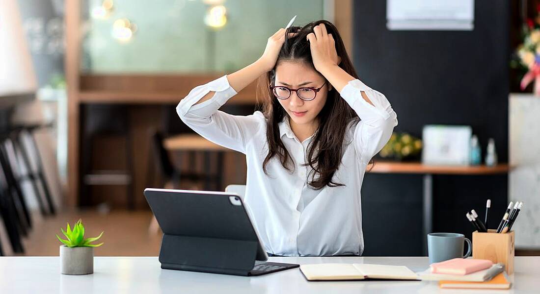 Woman working at a desk in an office space, looking stressed with her hands in her hair.